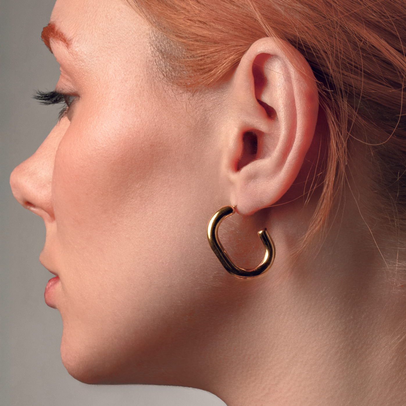 Pendientes Umami Gold de tubo curvado en baño de oro usados en modelo, ideales para looks originales y sofisticados.